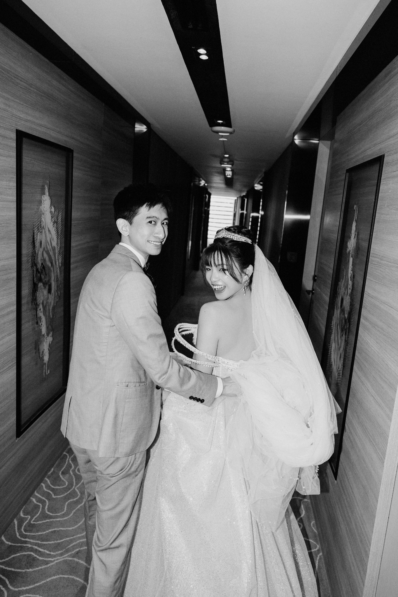 Newlyweds laughing together in a hotel corridor